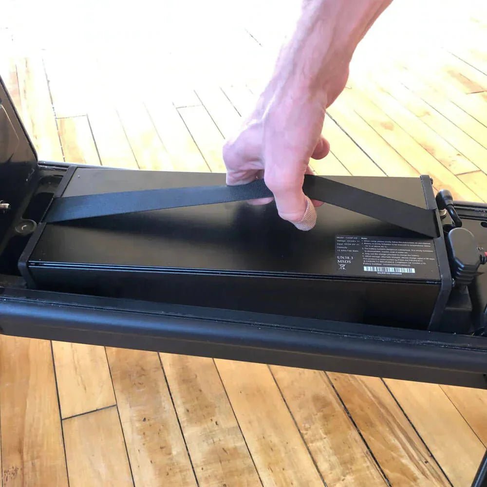 Mano che estrae per la cinghia la batteria removibile del monopattino, al chiuso: si ricarica meglio a temperatura ambiente