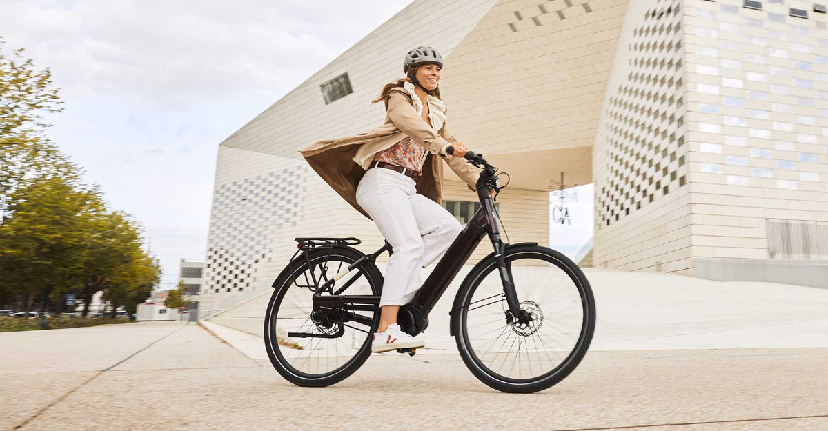 Donna con il casco in sella a una bici elettrica davanti a un edificio moderno – normativa sulla bici elettrica