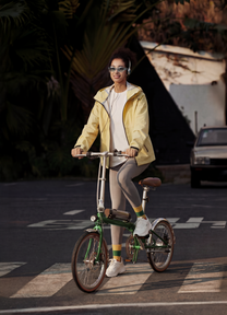 Donna alla guida della bici elettrica pieghevole OneSport OT02 Pro in colore verde in un ambiente serale