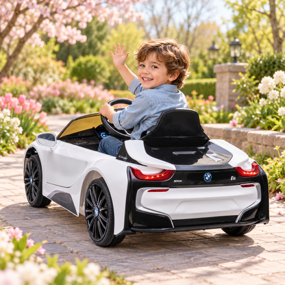 Bambino alla guida dell'auto elettrica per bambini BMW i8 Coupé in un parco, da un'altra angolazione