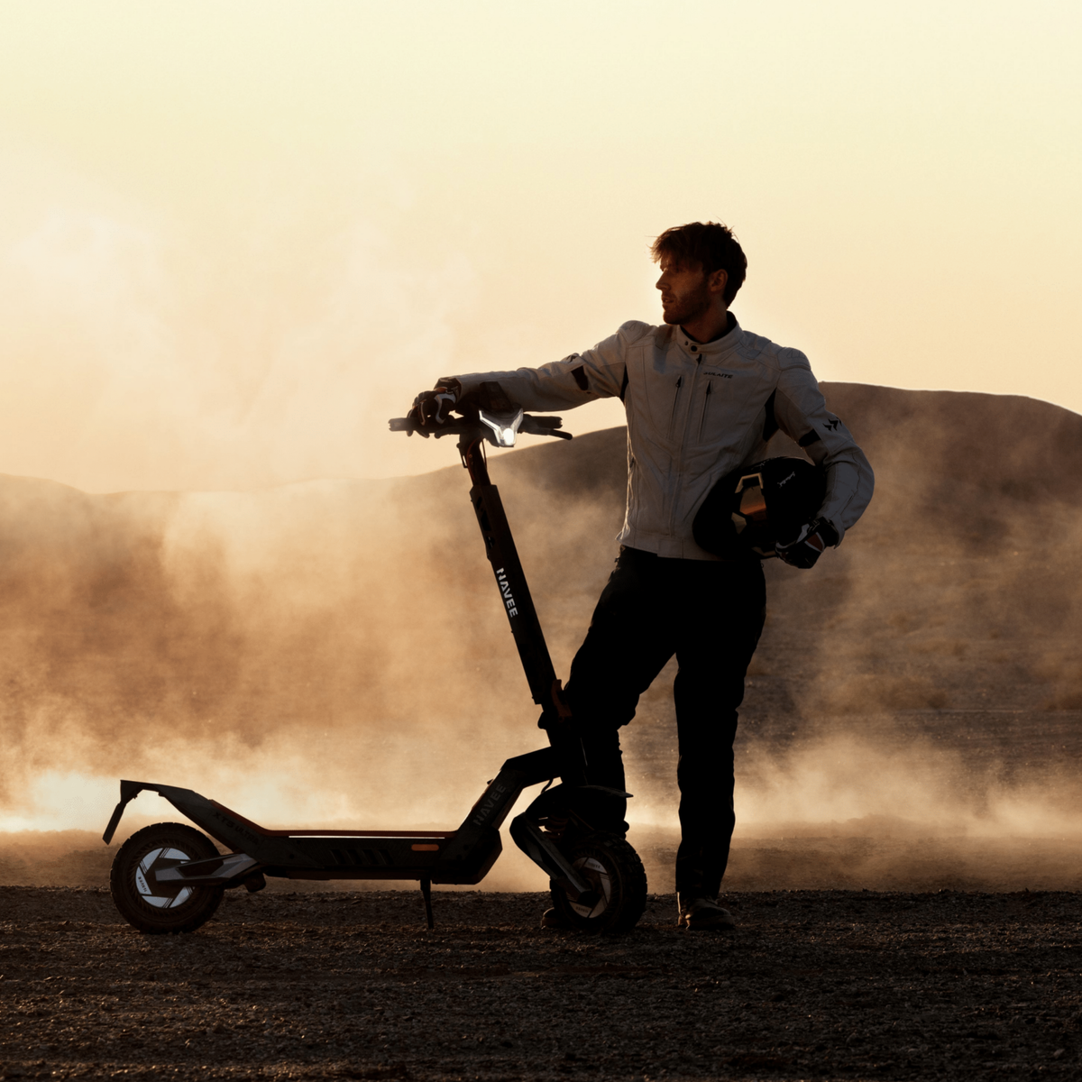 Persona in piedi con il monopattino elettrico NAVEE XT5 Max su terreno sabbioso al tramonto