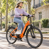Donna con casco in sella a una OneSport OT05 Max arancione su una strada con alberi e facciate
