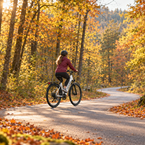 Donna con casco in bicicletta su una OneSport OT12 Pro bianca su una strada forestale tra foglie autunnali