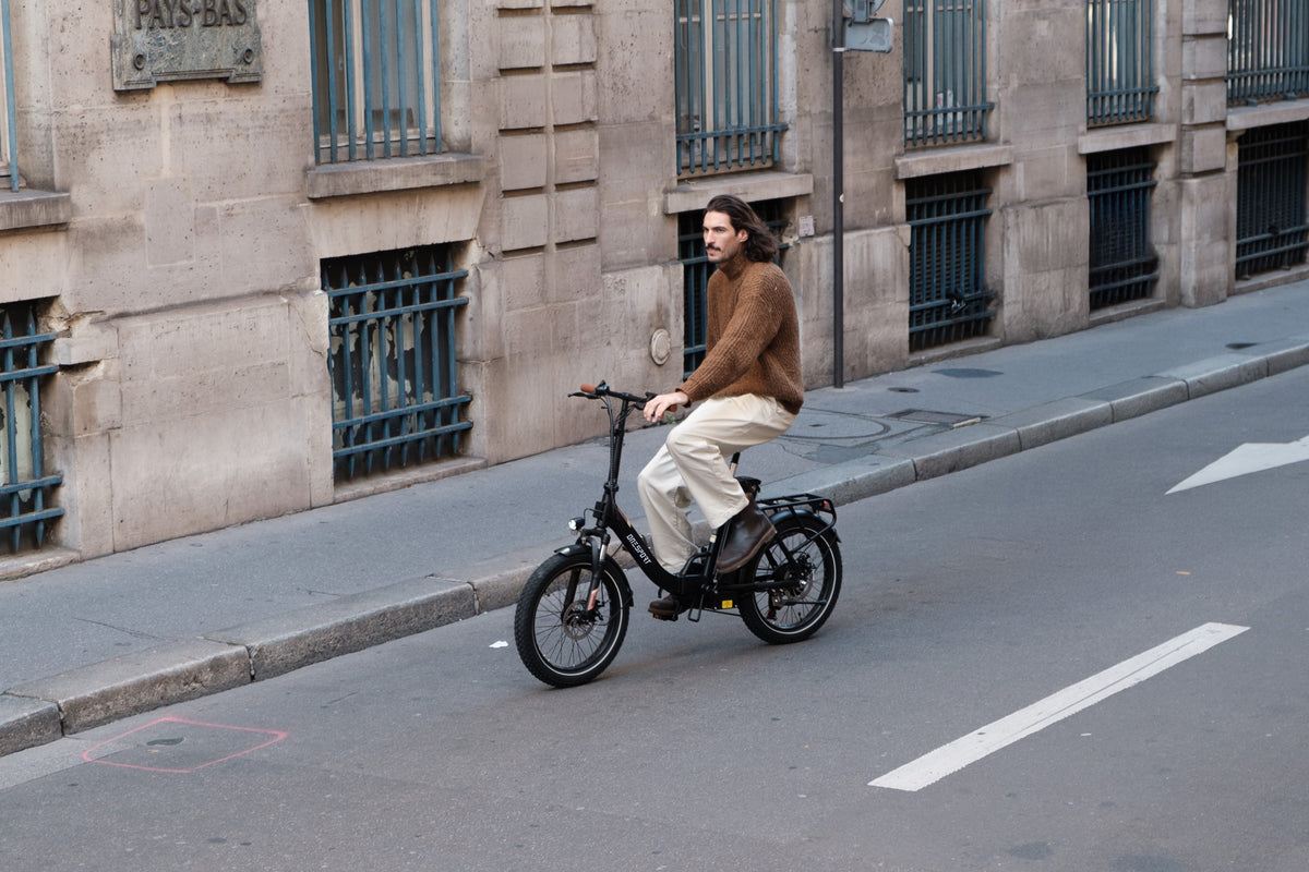 Uomo in sella a una OneSport OT16 Pro, bicicletta nera, su una strada lungo un edificio in pietra con inferriate alle finestre