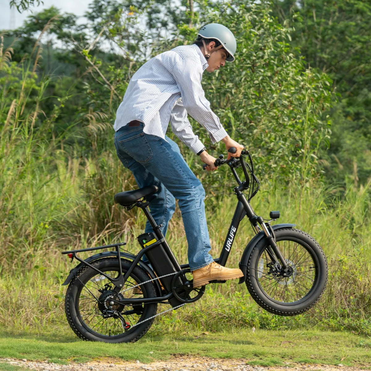 Uomo alla guida della fat bike elettrica URLIFE E20 in colore nero con il casco su un prato