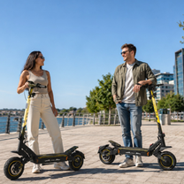 Una donna e un uomo in piedi, ciascuno accanto al proprio monopattino elettrico Wheely - H7, su una banchina vicino all'acqua