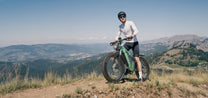 Uomo in piedi con la fat bike elettrica Duotts E26 su un prato in montagna