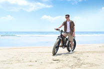 Uomo alla guida della fat bike elettrica Duotts S26 in riva al mare