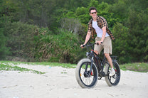 Uomo in piedi con la fat bike elettrica Duotts S26 in riva al mare