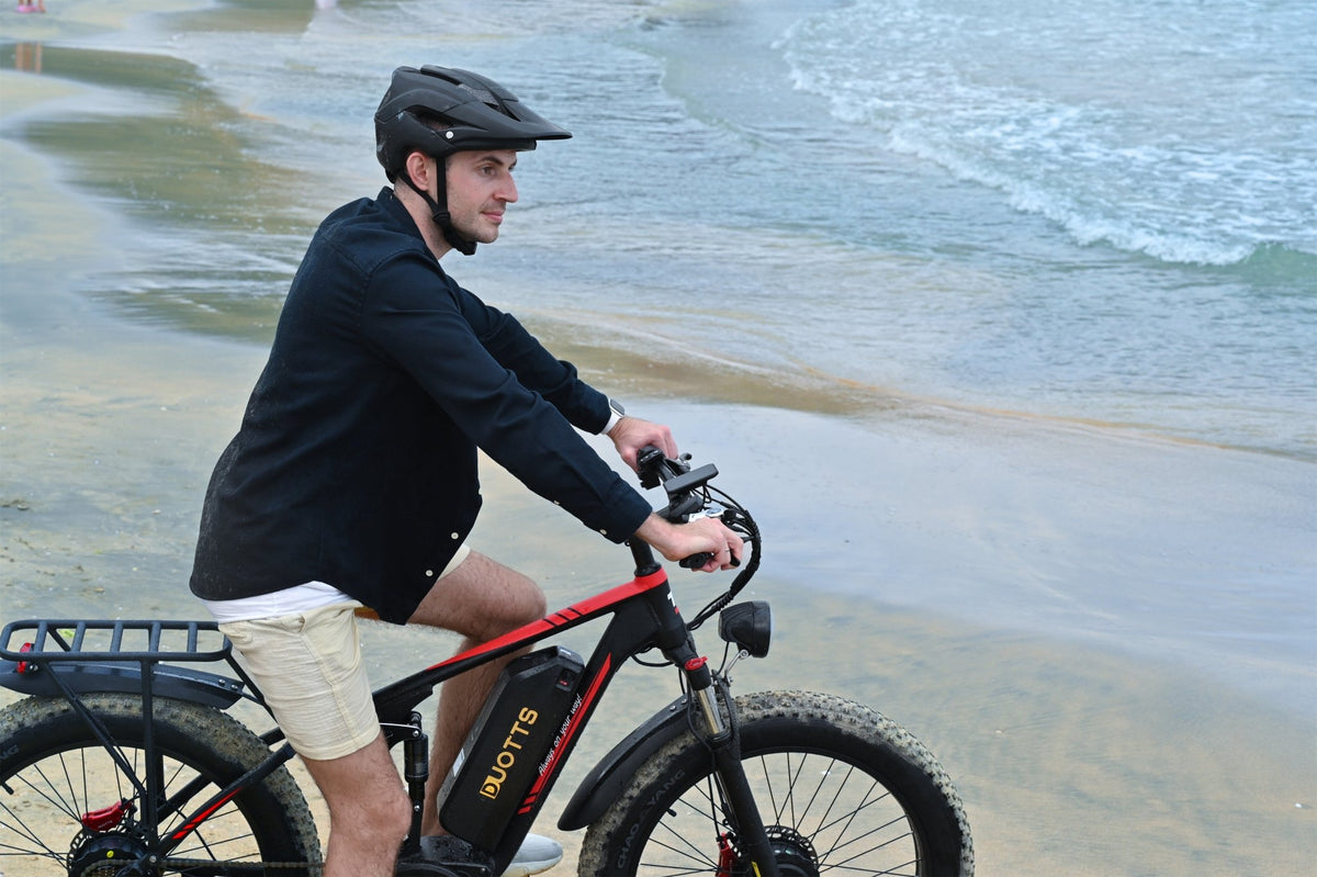 Uomo in piedi con la fat bike elettrica Duotts S26 in riva al mare