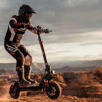 Persona in piedi con il monopattino elettrico iScooter GX3 Pro su terreno sabbioso al tramonto