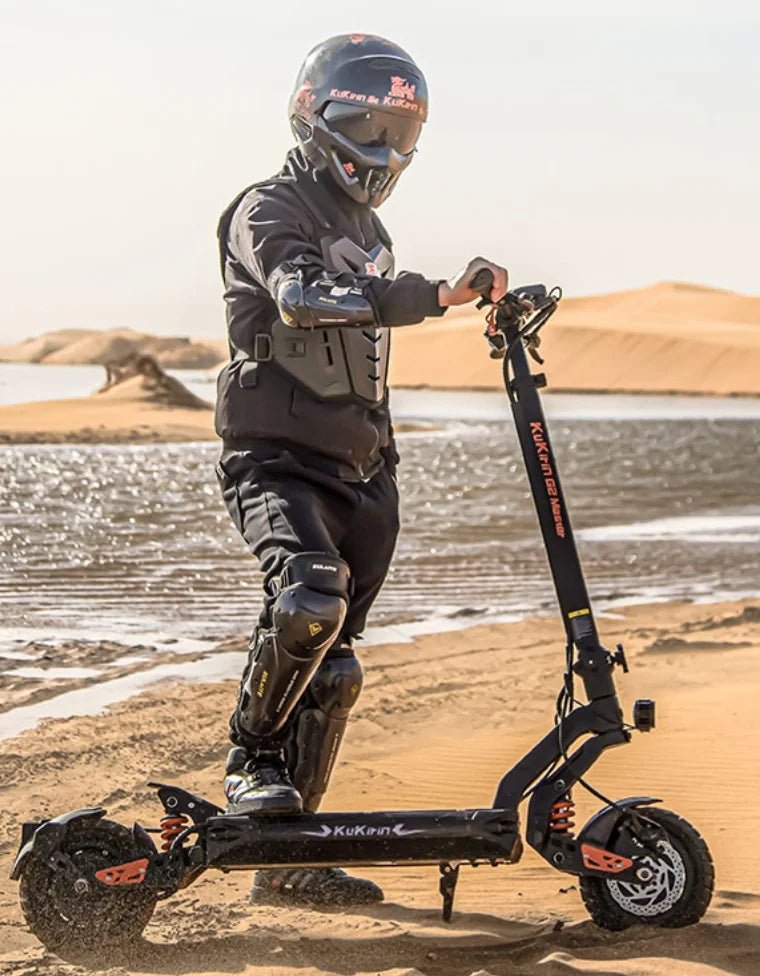 Persona in piedi con il monopattino elettrico KuKirin G2 Master con il casco su terreno sabbioso