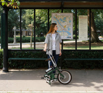 Donna in piedi con la bici elettrica pieghevole OneSport OT02 in città