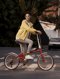 Donna alla guida della bici elettrica pieghevole OneSport OT02 Pro in colore rosso in una strada