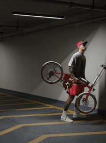 Persona in piedi con la bici elettrica pieghevole OneSport OT02 Pro in colore rosso al chiuso
