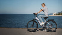 Persona alla guida della bici elettrica OneSport OT05 Pro con il casco in riva al mare in colore azzurro