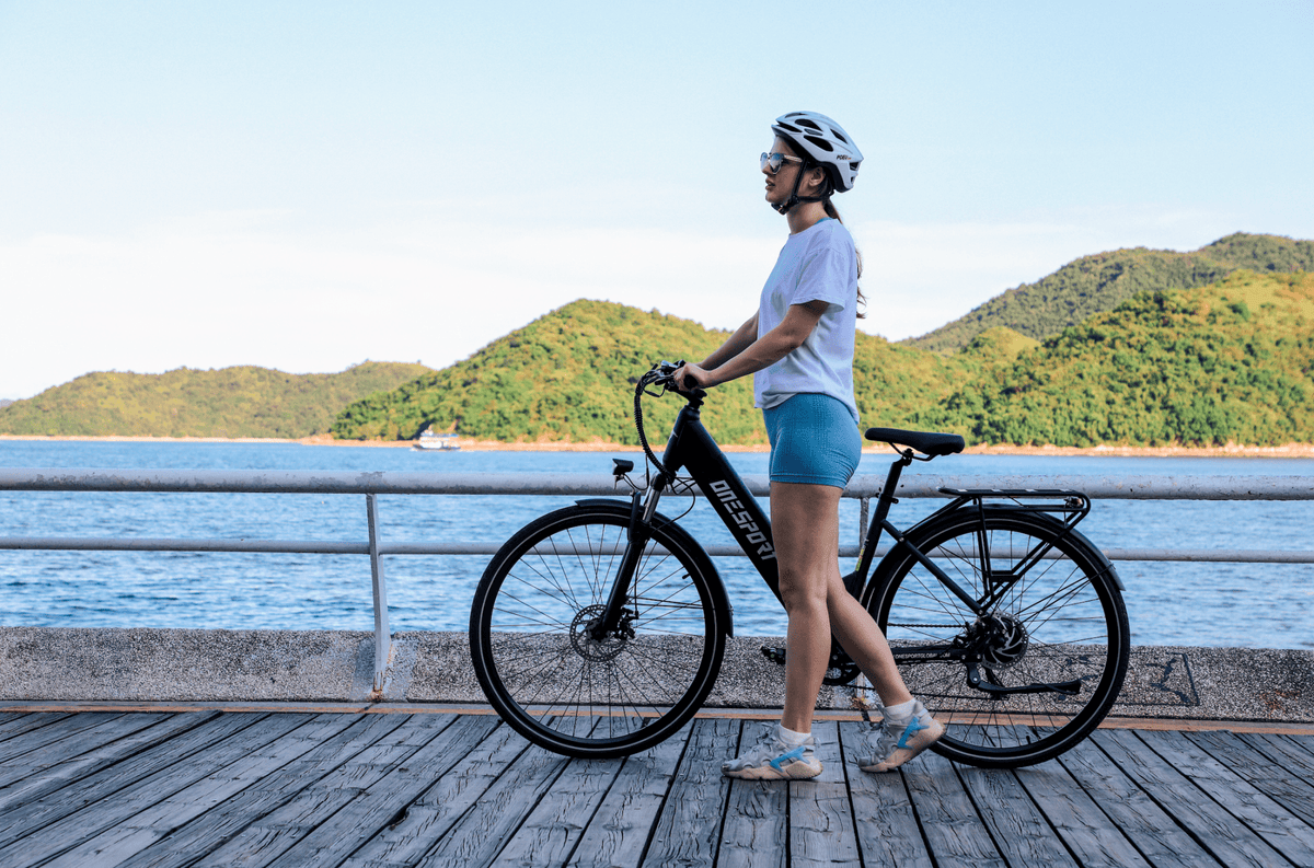 Donna in piedi con la bici elettrica OneSport OT12 in colore nero in riva al mare