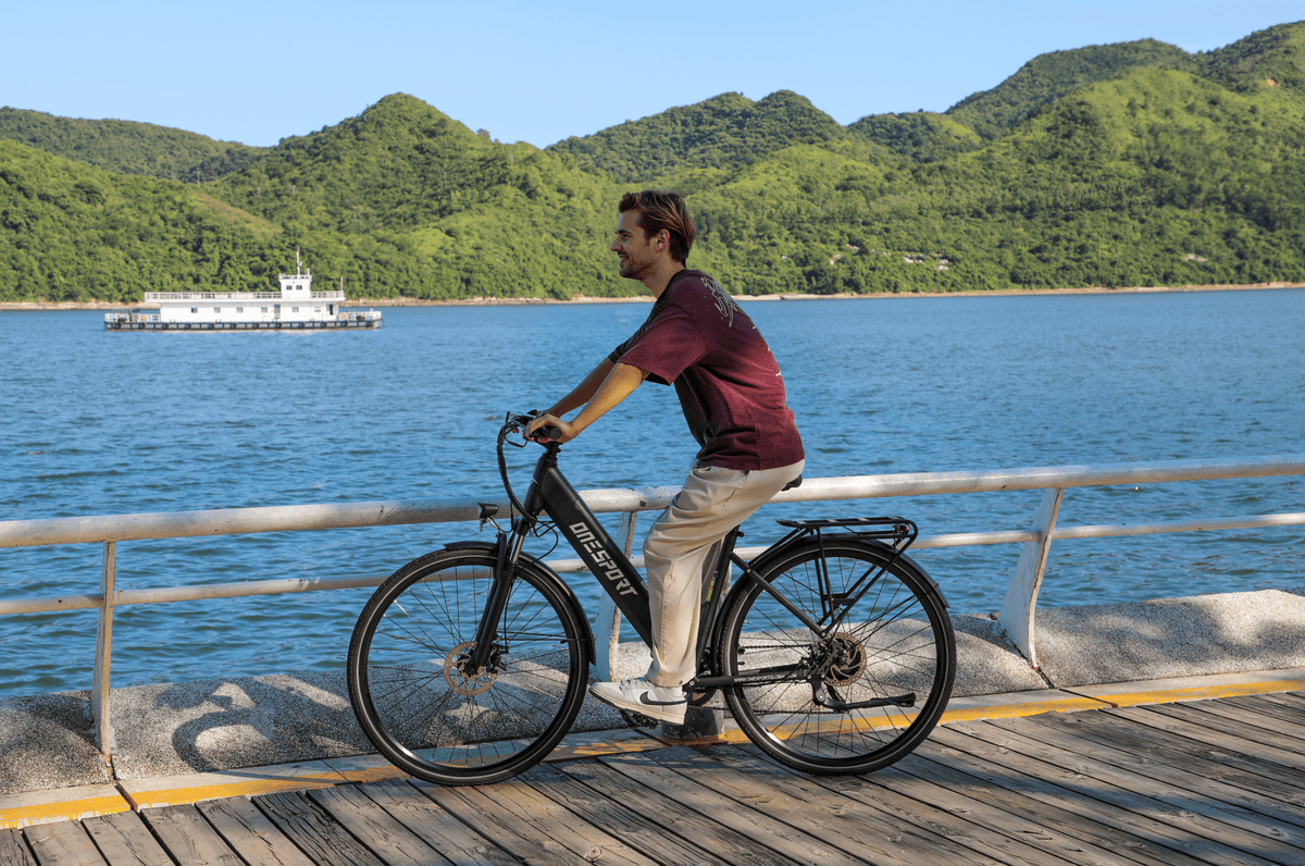 Persona alla guida della bici elettrica OneSport OT12 in colore nero in riva al mare