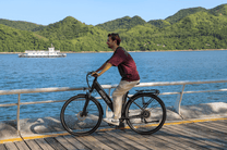 Persona alla guida della bici elettrica OneSport OT12 in colore nero in riva al mare
