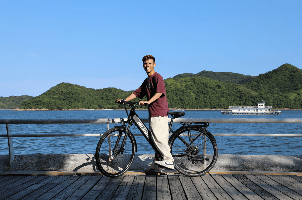 Uomo in piedi con la bici elettrica OneSport OT12 in colore nero in riva al mare