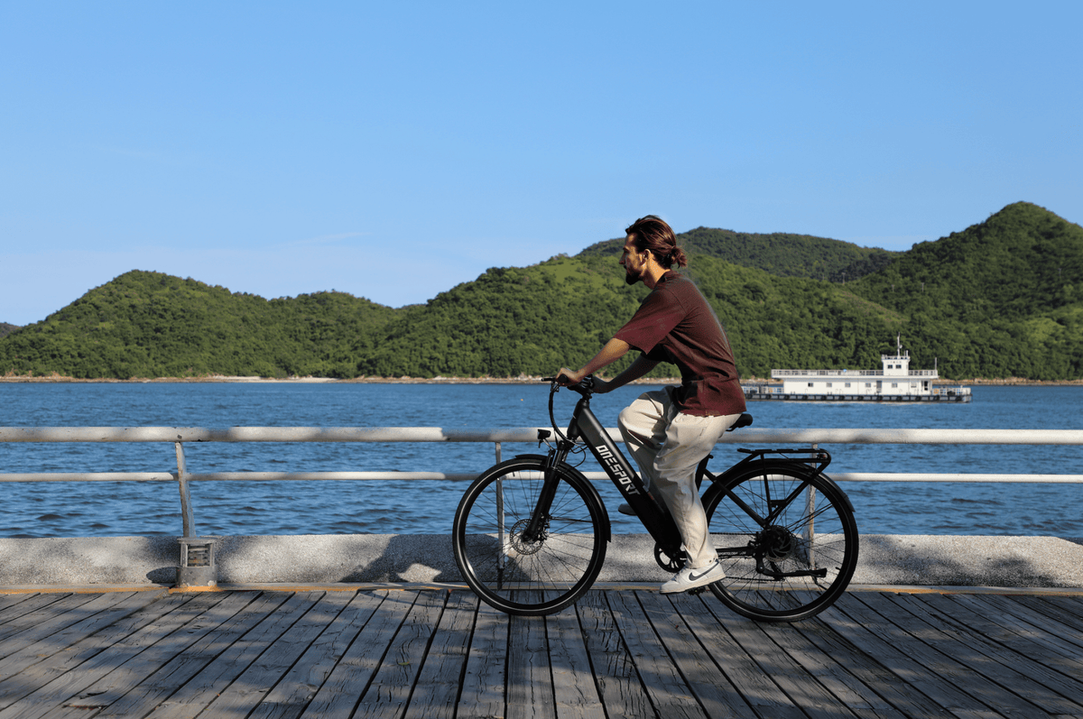 Uomo alla guida della bici elettrica OneSport OT12 in colore nero in riva al mare