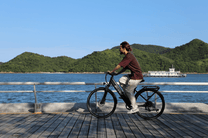 Uomo alla guida della bici elettrica OneSport OT12 in colore nero in riva al mare
