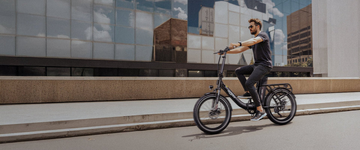 Uomo alla guida della bici elettrica pieghevole OneSport OT16-2 in colore nero in città