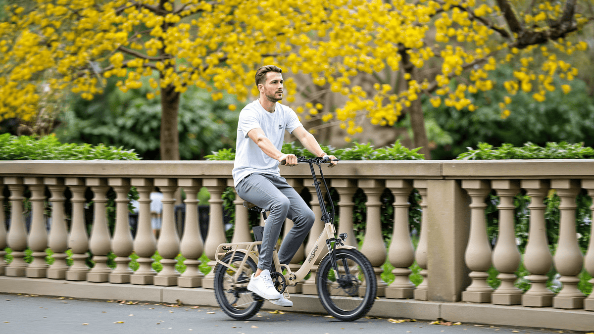 Uomo alla guida della bici elettrica pieghevole OneSport OT16-2 in colore beige in un parco