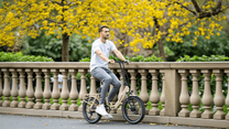 Uomo alla guida della bici elettrica pieghevole OneSport OT16-2 in colore beige in un parco