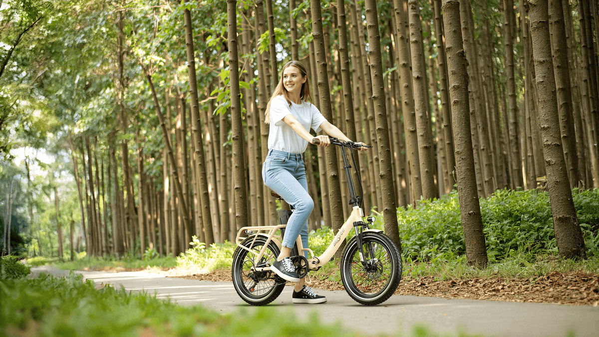 Donna alla guida della bici elettrica pieghevole OneSport OT16-2 in colore beige nel bosco