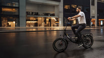 Uomo alla guida della fat bike elettrica pieghevole OneSport OT16 Max in colore nero in città al tramonto