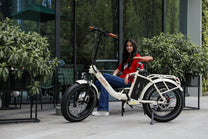 Donna in sella alla fat bike elettrica pieghevole OneSport OT16 Max in colore beige in una strada