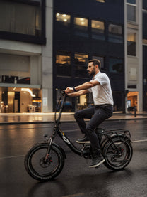 Uomo alla guida della fat bike elettrica pieghevole OneSport OT16 Max in colore nero in un ambiente serale