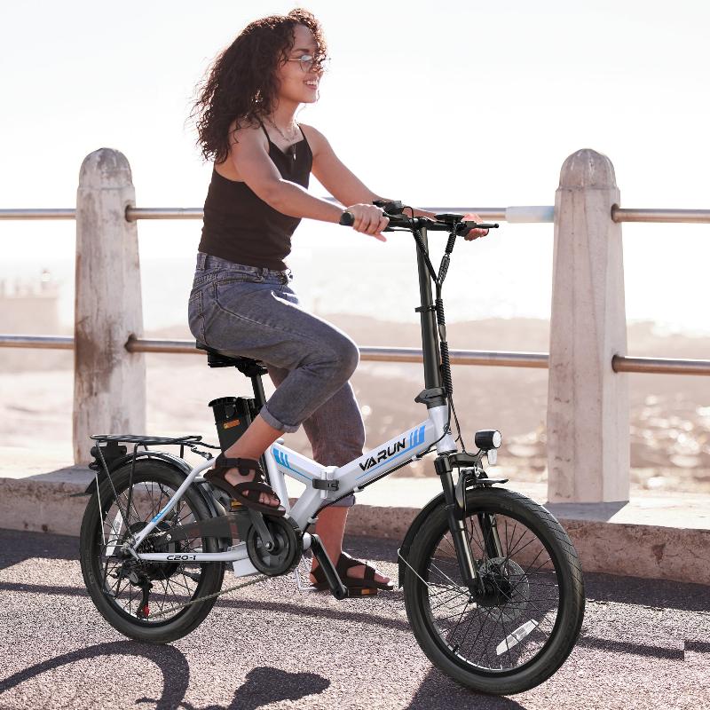 Donna alla guida della bici elettrica pieghevole VARUN C20-1 Pro in colore bianco su un vialetto