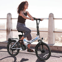 Donna alla guida della bici elettrica pieghevole VARUN C20-1 Pro in colore bianco su un vialetto