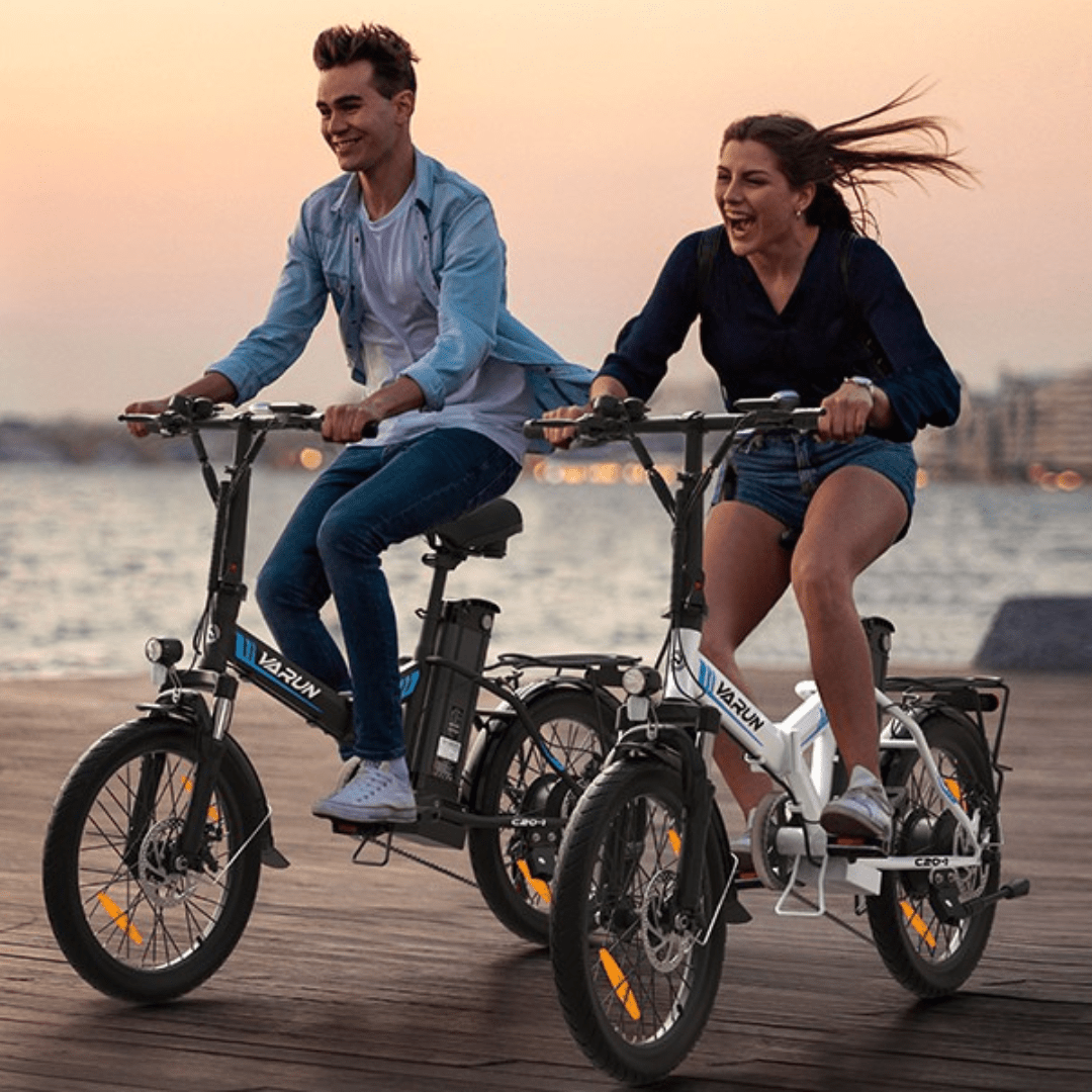 Due persone con la bici elettrica pieghevole VARUN C20-1 Pro in riva a un lago al tramonto