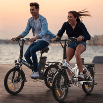 Due persone con la bici elettrica pieghevole VARUN C20-1 Pro in riva a un lago al tramonto