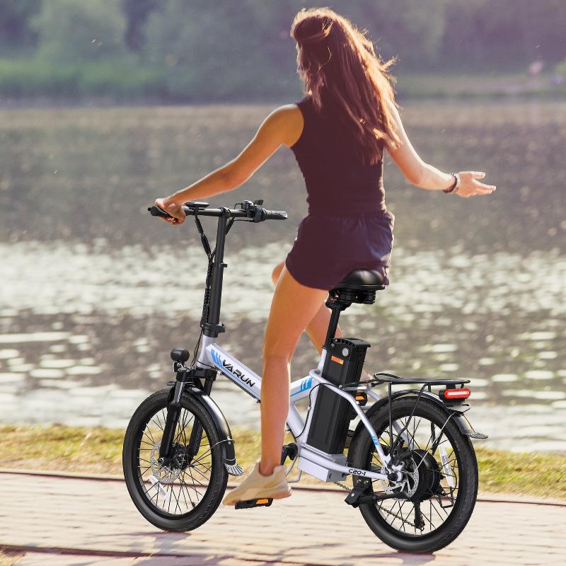 Donna alla guida della bici elettrica pieghevole VARUN C20-1 Pro in colore bianco in riva a un lago
