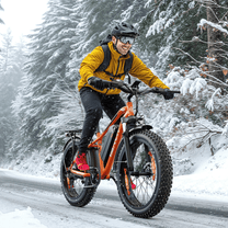 Uomo alla guida della fat bike elettrica VARUN M26-2 Plus in colore arancione con il casco sulla neve