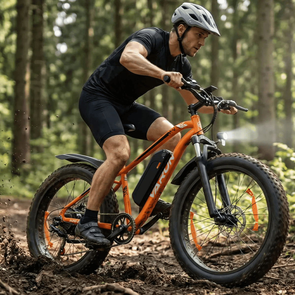 Uomo alla guida della fat bike elettrica VARUN M26-2 Pro in colore arancione con il casco nel bosco