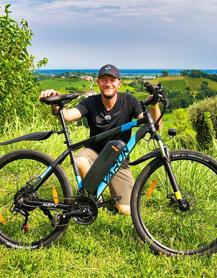 Uomo in piedi con la mountain bike elettrica VARUN M27-1 Pro in colore blu su un prato