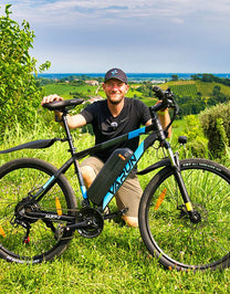Uomo in piedi con la mountain bike elettrica VARUN M27-1 Pro in colore blu su un prato