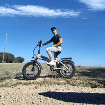 Uomo alla guida della fat bike elettrica pieghevole VARUN S20-1 in colore beige su una strada sterrata