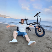 Persona seduta accanto alla fat bike elettrica pieghevole VARUN S20-1 in colore nero in riva al mare