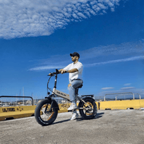 Uomo alla guida della fat bike elettrica pieghevole VARUN S20-1 in colore beige in riva al mare