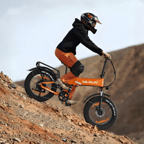 Uomo alla guida della fat bike elettrica pieghevole VARUN S20-1 Plus in colore arancione con il casco nel deserto