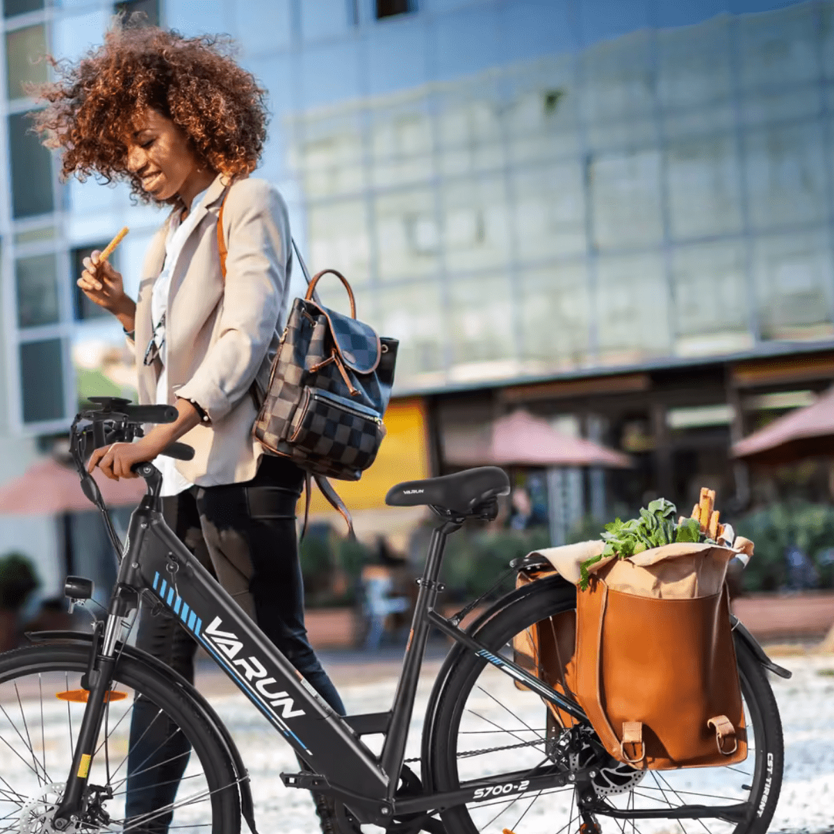 Donna in piedi con la bici elettrica VARUN S700-2 in colore nero con cestino posteriore in città