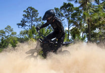 Persona in piedi con la moto da cross elettrica Vipcoo H3 nel bosco