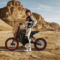 Persona in piedi con la moto da cross elettrica Wheely Y01 su terreno sabbioso